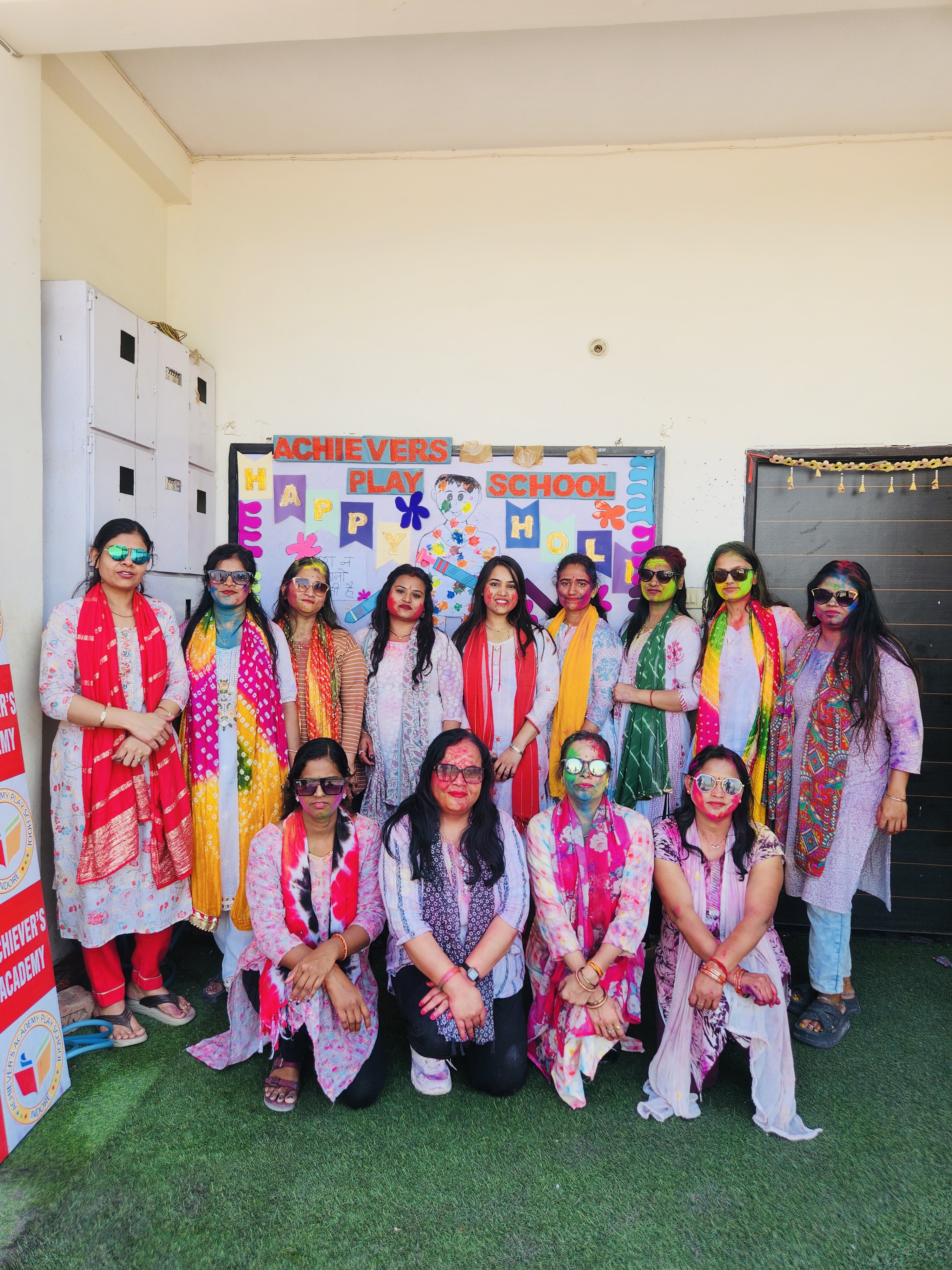 Holi Celebration - School teachers and staff with color on faces in front of Holi banner